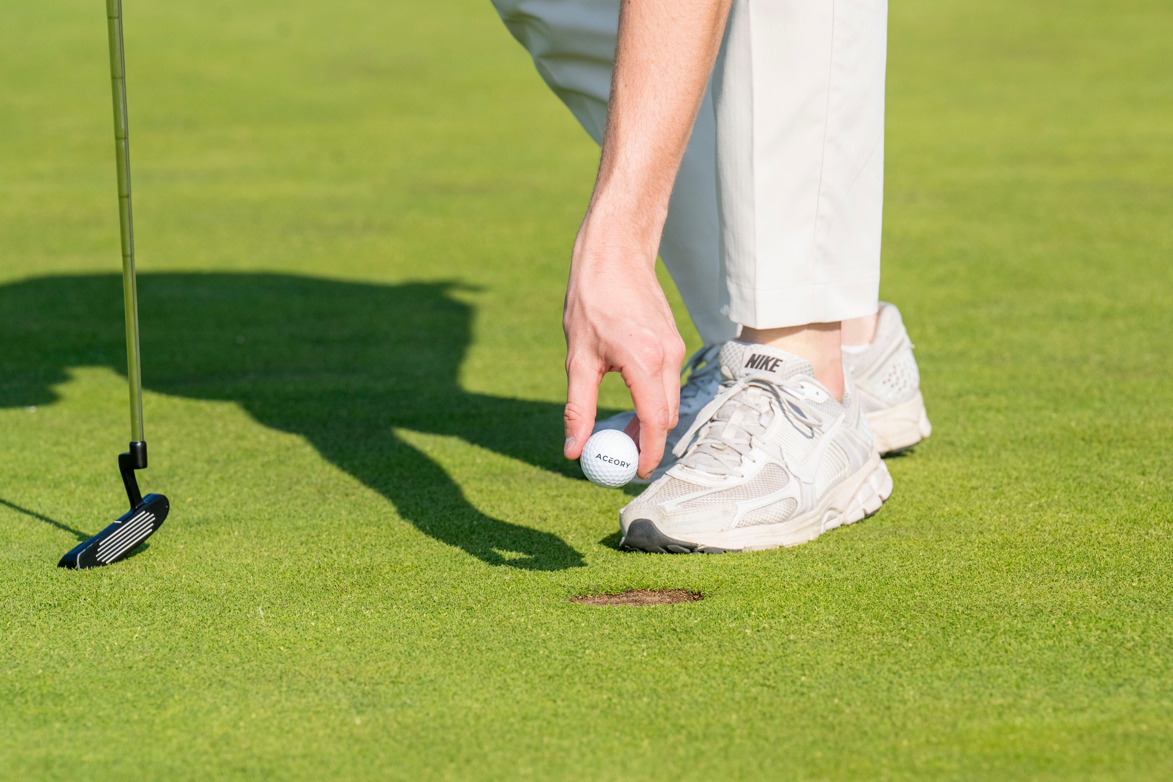 Person on a golf course preparing to putt with a putter and golf ball.