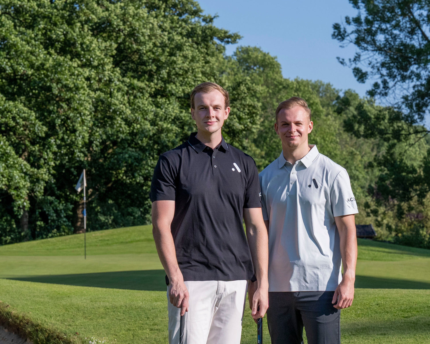 Two men standing on a golf course with trees in the background