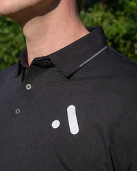 Outdoor close-up of the Aceory logo on a black essentials polo.