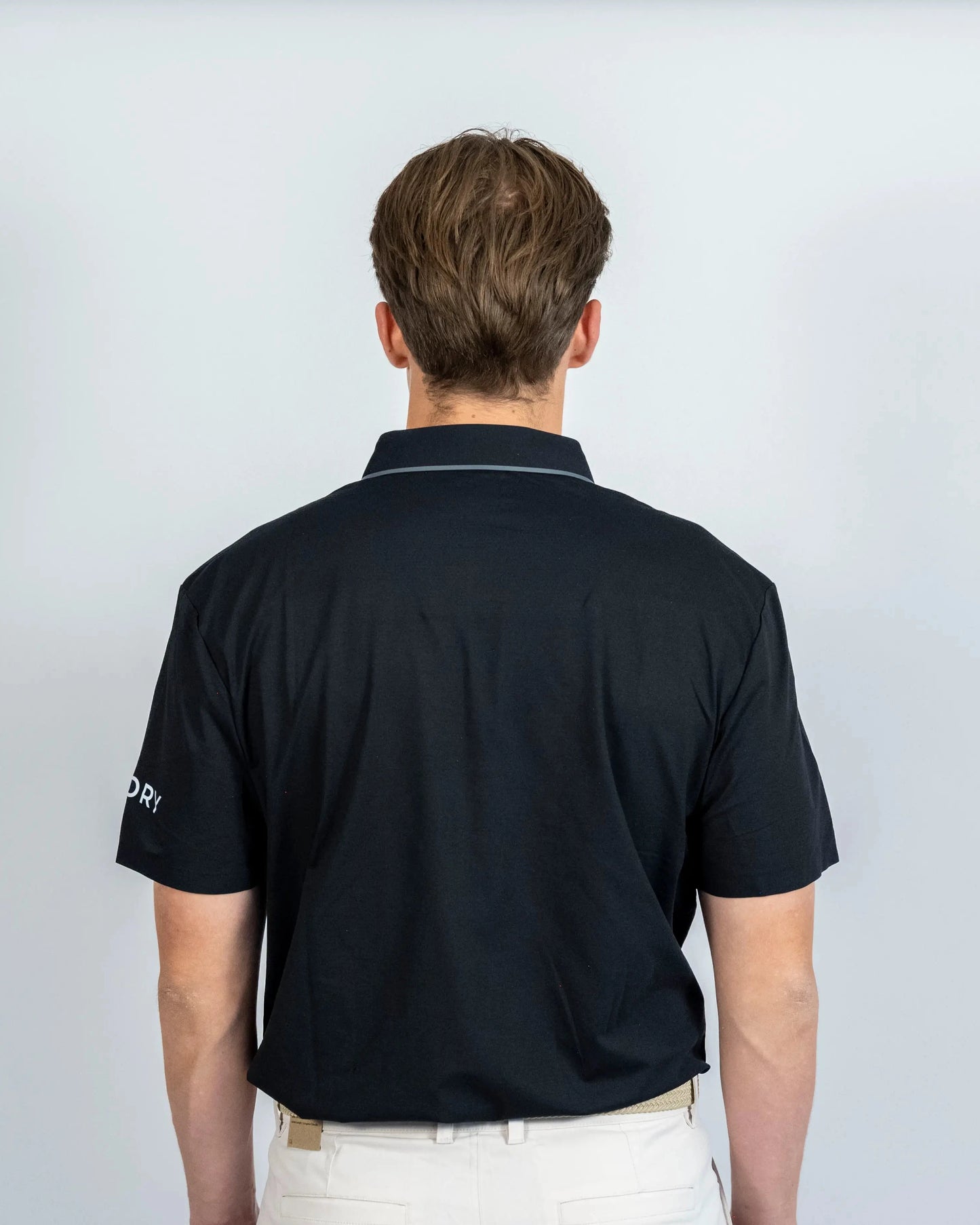 Back view of model wearing the black Aceory performance polo in studio.