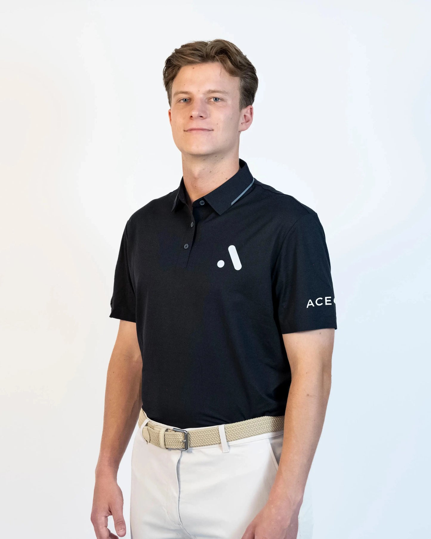 Three-quarter view of model wearing the black Aceory performance polo with beige golf trousers.