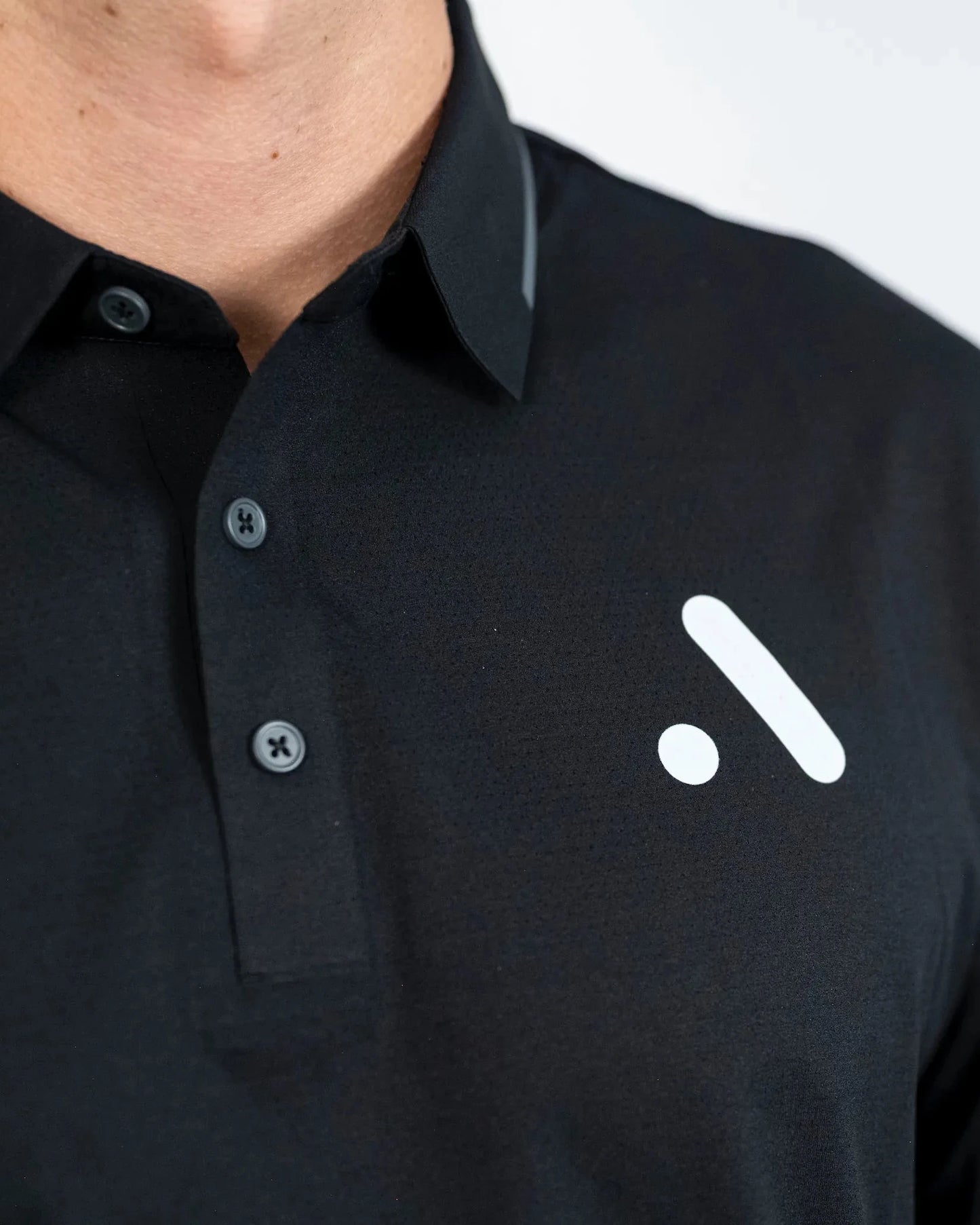 Close-up of the Aceory logo on the chest of the black Aceory Essentials polo showing collar and buttons.