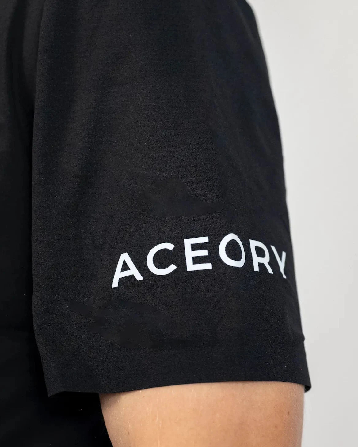 Close-up of the Aceory logo printed on the sleeve of the black Aceory Essentials golf polo.