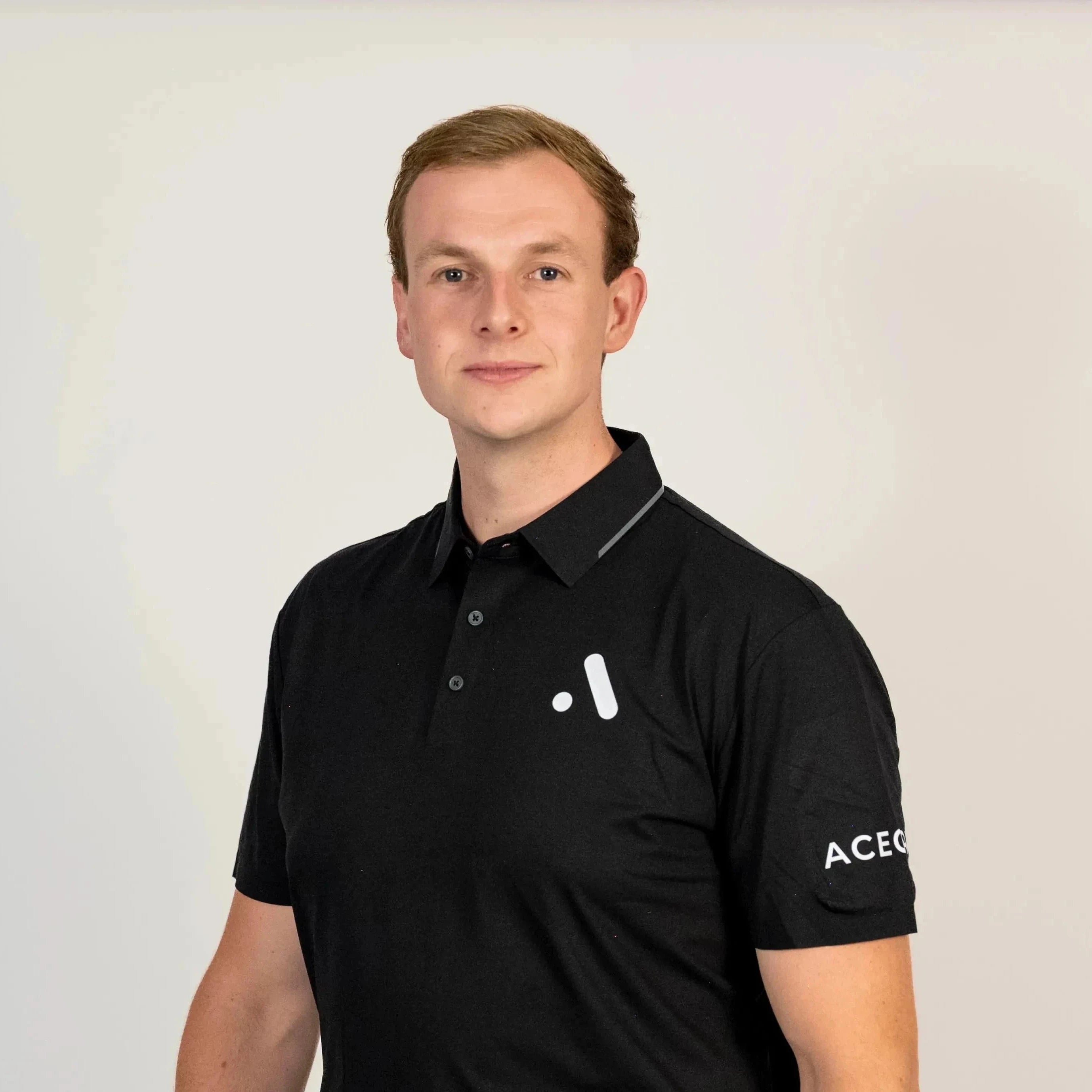 Model wearing the black Aceory Essentials polo with beige trousers, studio lighting and neutral background.