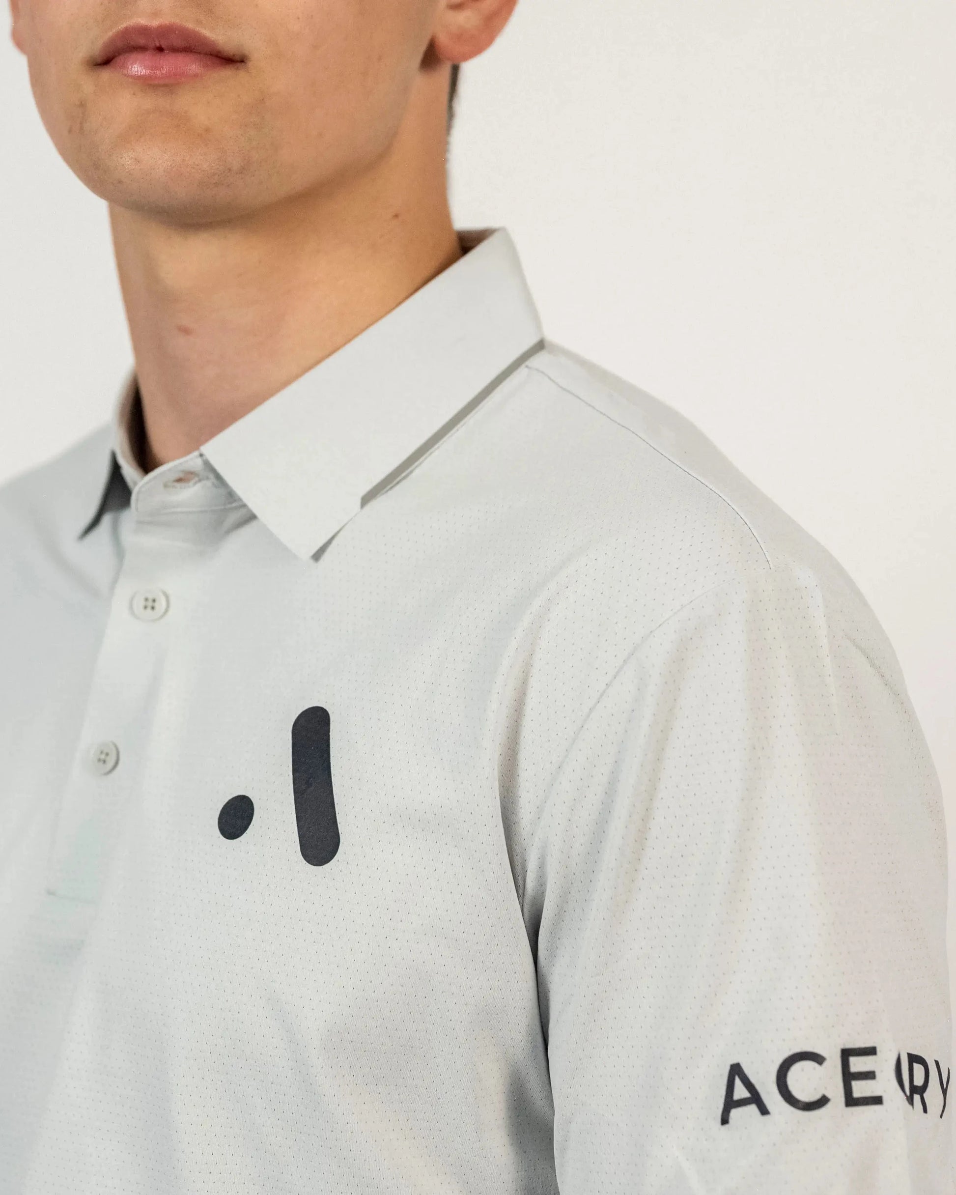 Close-up of the black Aceory logo on the chest of the light grey Aceory Essentials polo.