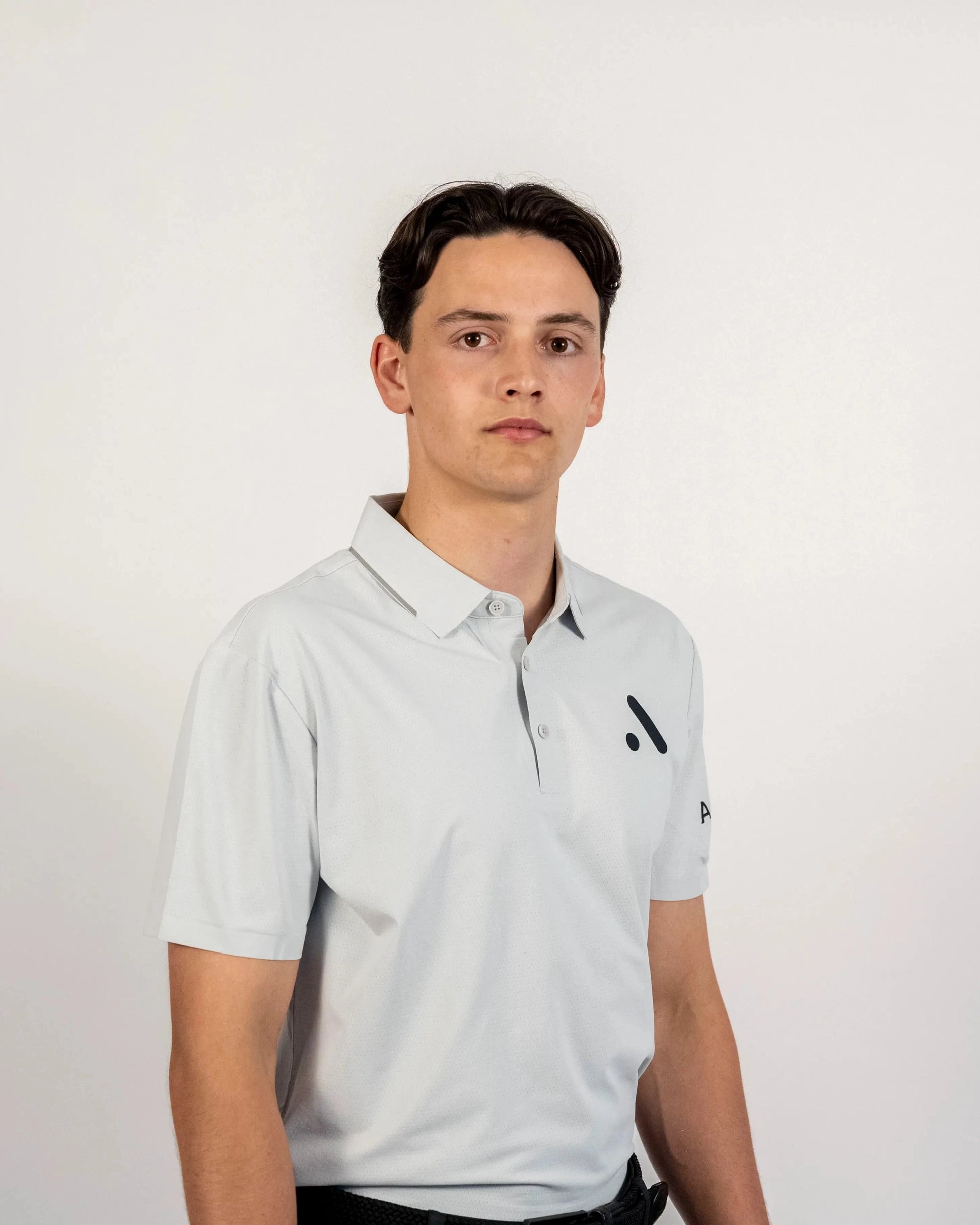 Three-quarter front studio view of a model wearing the light grey Aceory Essentials polo with dark trousers.