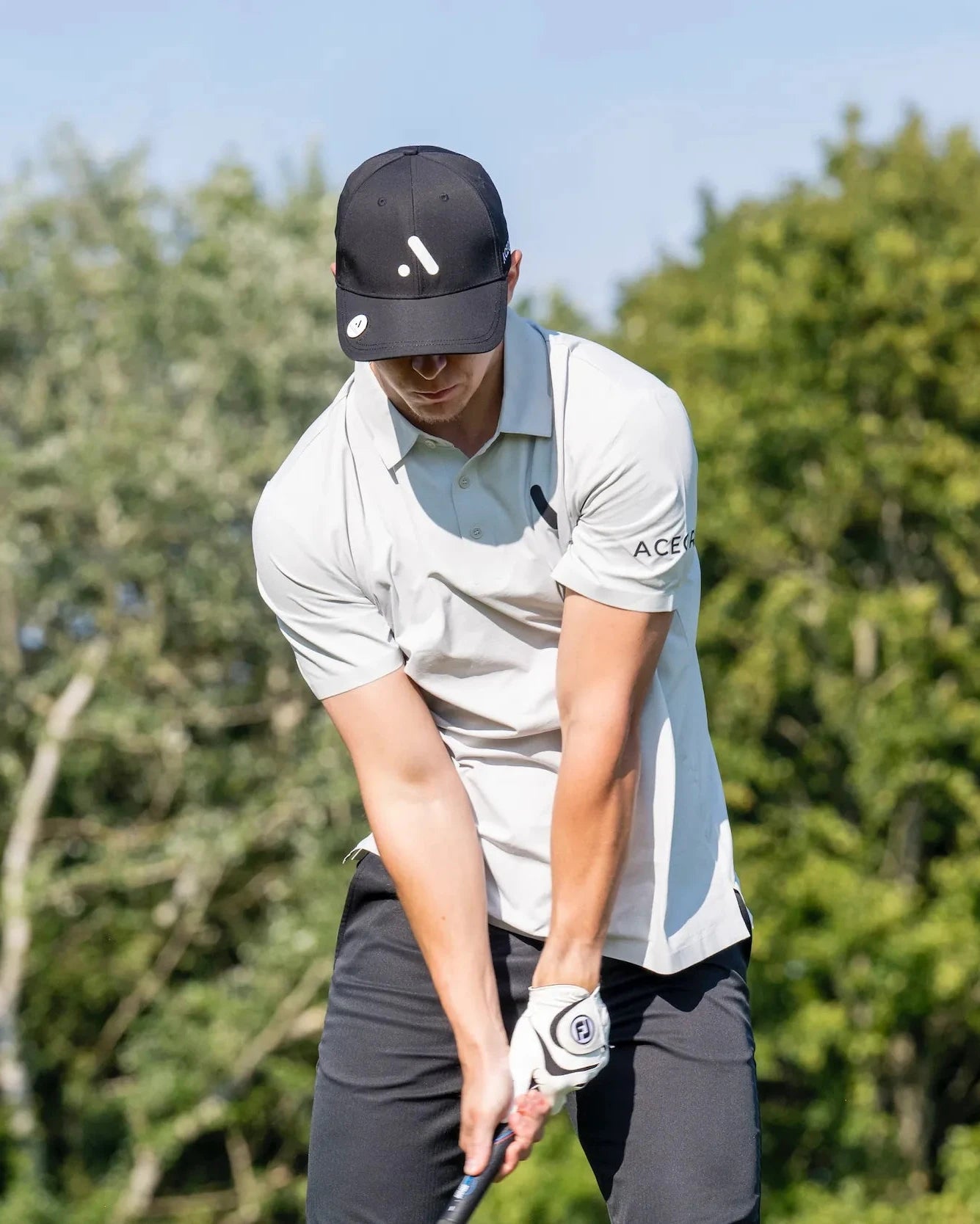 Golfer preparing to swing while wearing light grey Aceory Essentials polo and black pants.