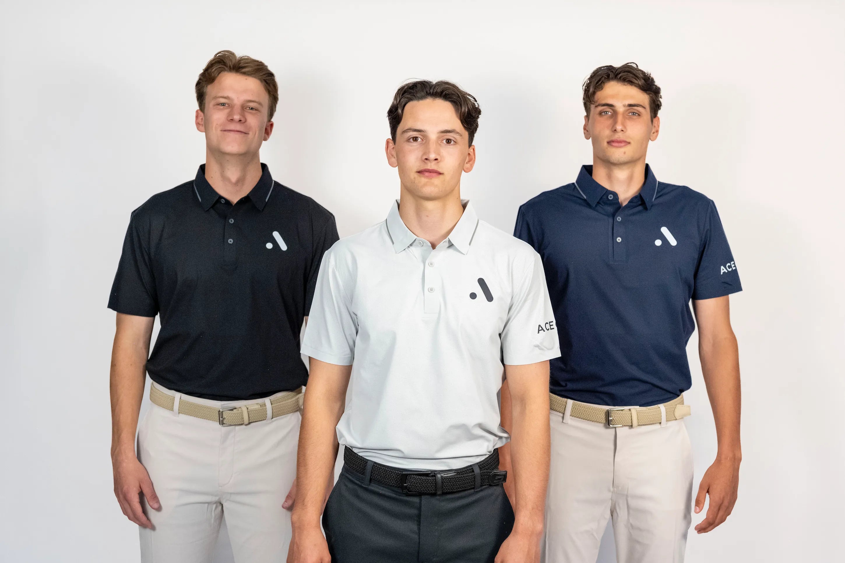 Three models wearing Aceory Essentials polos in black, navy, and light grey standing side by side in studio.
