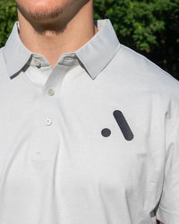 Outdoor close-up of the Aceory logo on a light grey essentials polo.