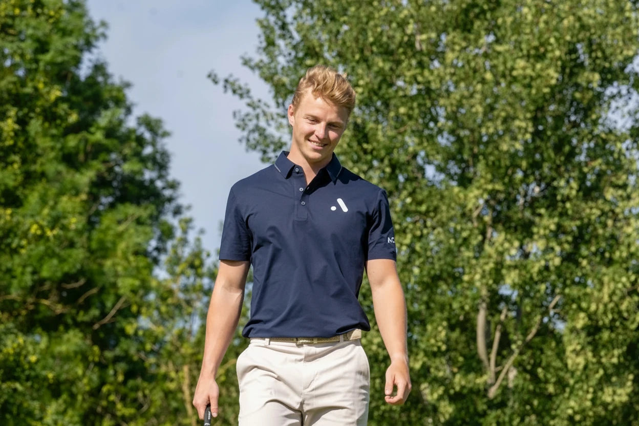 Male golfer wearing the navy Aceory Essentials Polo walking on the green